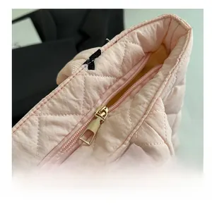 Macro view of smooth light gold zipper and quilted diamond pattern on pink tote bag