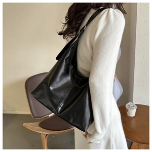 Close-up of black glossy faux leather shoulder bag with vertical stitching detail