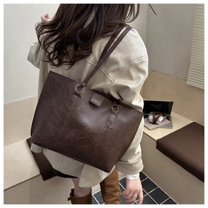 Brown large capacity leather tote bag shown on a model in a minimal office setting