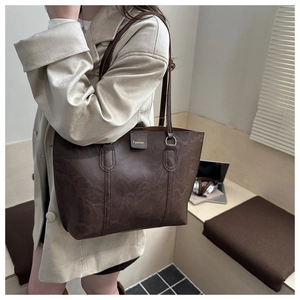 Detail of a large dark brown marble-textured tote bag with gold lettering shown on a model