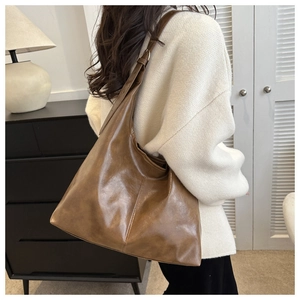Detailed view of spacious brown leather tote bag worn on shoulder in a home setting
