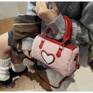 Detail der rosa Plüschtextur und des roten Leder Herz-Aufnähers an einer Boston-Handtasche