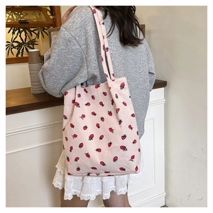 Dettaglio della borsa tote rosa in velluto a coste con motivi fragola indossata dal modello