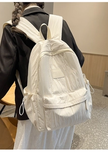 Detail of a minimalist white textured backpack featuring a brand patch and drawstring pockets