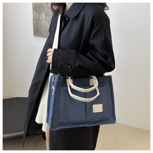 Détail du sac cabas en toile bleue avec poignées crème et écusson de la marque