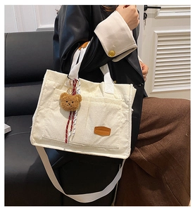 Detail view of corduroy tote bag with bear charm and wide strap on leather jacket