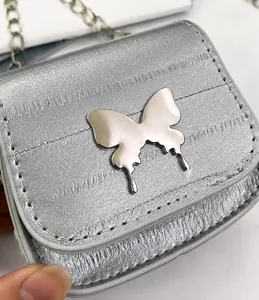 Detalle de mini bolso plateado mate con mariposa metálica y fina correa de cadena