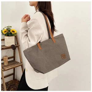 Primer plano detallado del bolso tote de lona gris oscuro con asas de cuero marrón y parche
