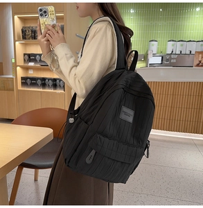 Detailed side view of black crinkled nylon backpack with adjustable straps in cafe