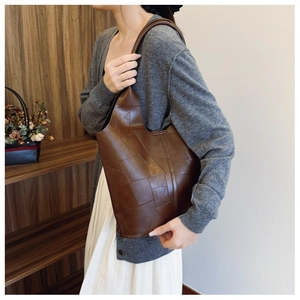 Detail of dark brown patchwork leather tote bag featuring matte texture and wide shoulder strap