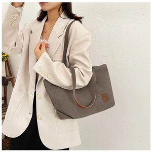 Detalle del gran bolso tote de lona gris con correa marrón llevado por una modelo