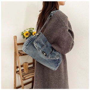 Detail view of retro denim shoulder bag with silver chain strap worn by a female model