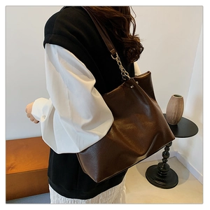 Détail d'un grand sac cabas marron foncé avec texture brillante et bandoulière chaîne dorée