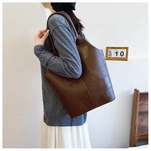 Detail view of brown leather tote bag with geometric embossed texture on model's shoulder