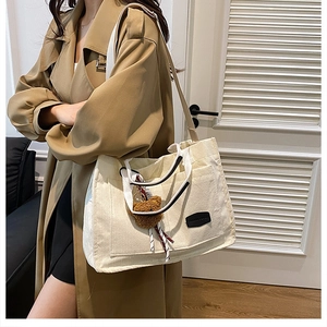 Close-up of beige corduroy tote bag with plush bear charm and fashion logo label
