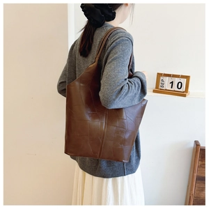 Detail of a large brown tote bag with geometric patchwork design and sleek leather texture