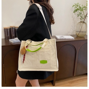 Close-up of beige corduroy tote bag with green accents, wide strap and cute bear charm