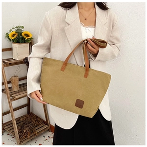 Dettaglio della borsa tote in tela kaki con manici in pelle marrone e logo patch