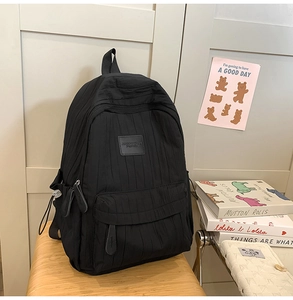 Detail of black backpack showing vertical pleated texture and front zipper pocket