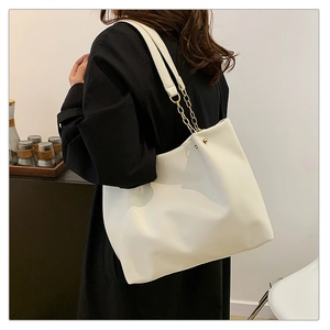 Détail du grand sac cabas blanc avec chaîne dorée porté sur un manteau noir chic