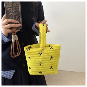Dettaglio di una borsa a secchiello gialla trapuntata con ricami di fiocchi neri
