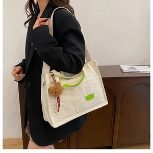 Detail of off-white corduroy tote bag with green straps and a plush bear pendant