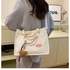 Close-up of cream corduroy tote bag with pink badge, bear charm, and white strap