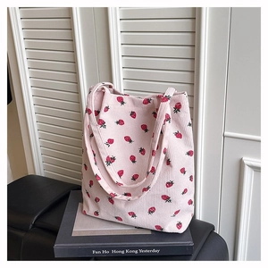Dettaglio della borsa tote in velluto a coste rosa con stampa di fragole rosse su un libro