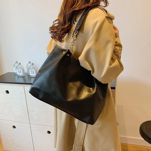 Sac fourre-tout minimaliste en cuir noir avec bandoulière en chaîne dorée porté