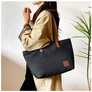 Dettaglio della borsa tote in tela nera con etichetta in pelle marrone e manici lunghi
