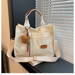 Detailed texture of corduroy tote bag with bear charm and wide strap in beige