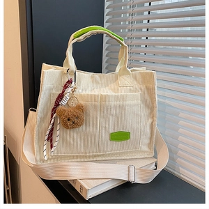 Detail of off-white corduroy tote bag featuring green logo tag and plush bear charm
