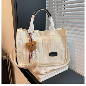 Detail of off-white corduroy tote bag with plush bear charm and fashion label