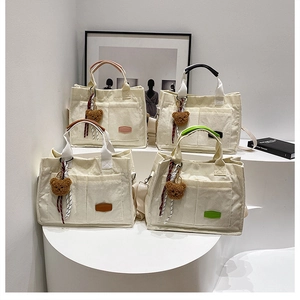Detail view of ivory corduroy tote bags with dual front pockets and plush bear charms