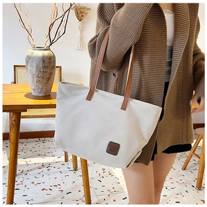 Dettaglio della borsa tote in tela beige con etichetta in pelle sul modello