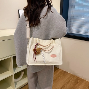 Off-white corduroy tote bag with wide strap and teddy bear charm shown on model