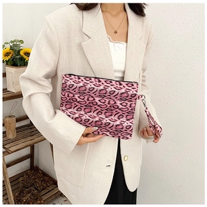 Pink leopard print clutch bag with wrist strap held by a model in a light blazer