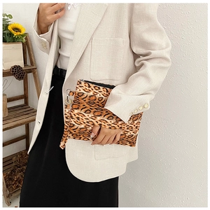 Detail of leopard print clutch with wrist strap and zipper on a beige suit
