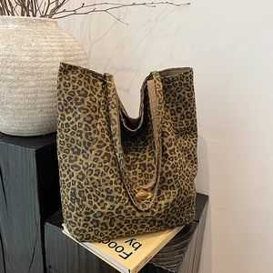Detail of leopard print canvas tote bag with a golden metal logo on a minimalist background