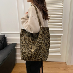 Detail view of leopard print canvas tote bag with gold handmade metal logo on a model
