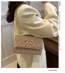 Close-up of beige quilted crossbody bag with golden metal bow buckle and chain strap detail