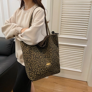 Macro detail of leopard print canvas tote bag featuring an oval gold metal logo plaque