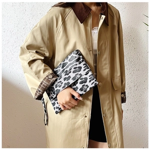 Detail shot of leopard print clutch bag held by model wearing a khaki trench coat