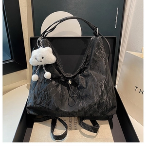 Detail of black pleated tote bag with cloud plush pendant and textured fabric surface