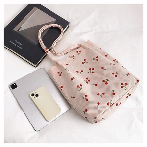Vista piatta di borsa tote in velluto a coste rosa con ciliegie e accessori