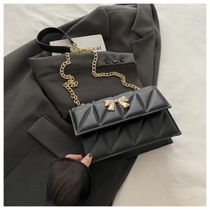 Detail of black quilted leather shoulder bag with a gold bow buckle and metal chain strap