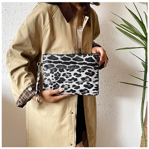 Detailed shot of leopard print clutch with silver zipper and wrist strap on khaki coat
