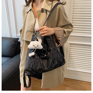 Detail of glossy black pleated tote bag featuring a cute white cloud plush pendant