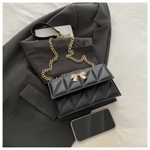 Detail of black quilted leather shoulder bag with elegant golden bow buckle and chain strap