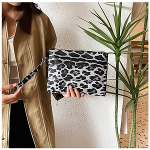 Detail of leopard print clutch bag with wristlet strap held against a trench coat